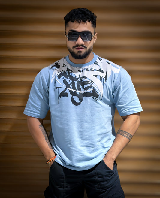 Man wearing a light blue t-shirt with a graphic design against a wooden background