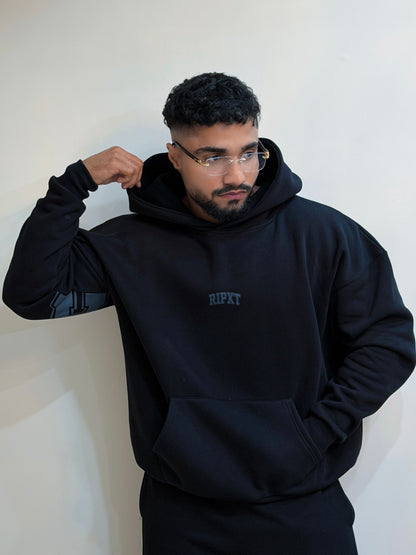 Man wearing a black hoodie with 'RIPXT' logo against a white wall