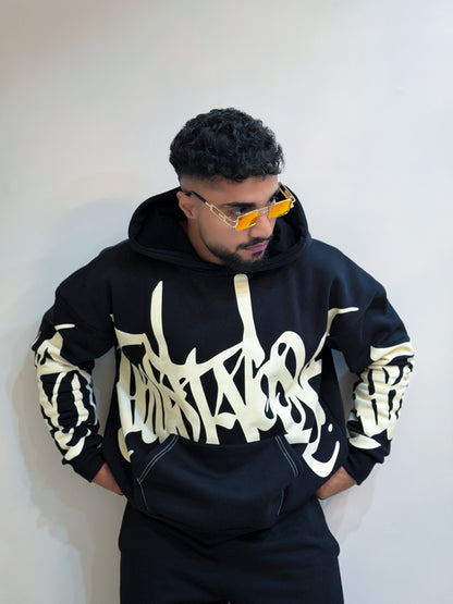 Person wearing a black hoodie with white text and patterns, standing against a plain background.