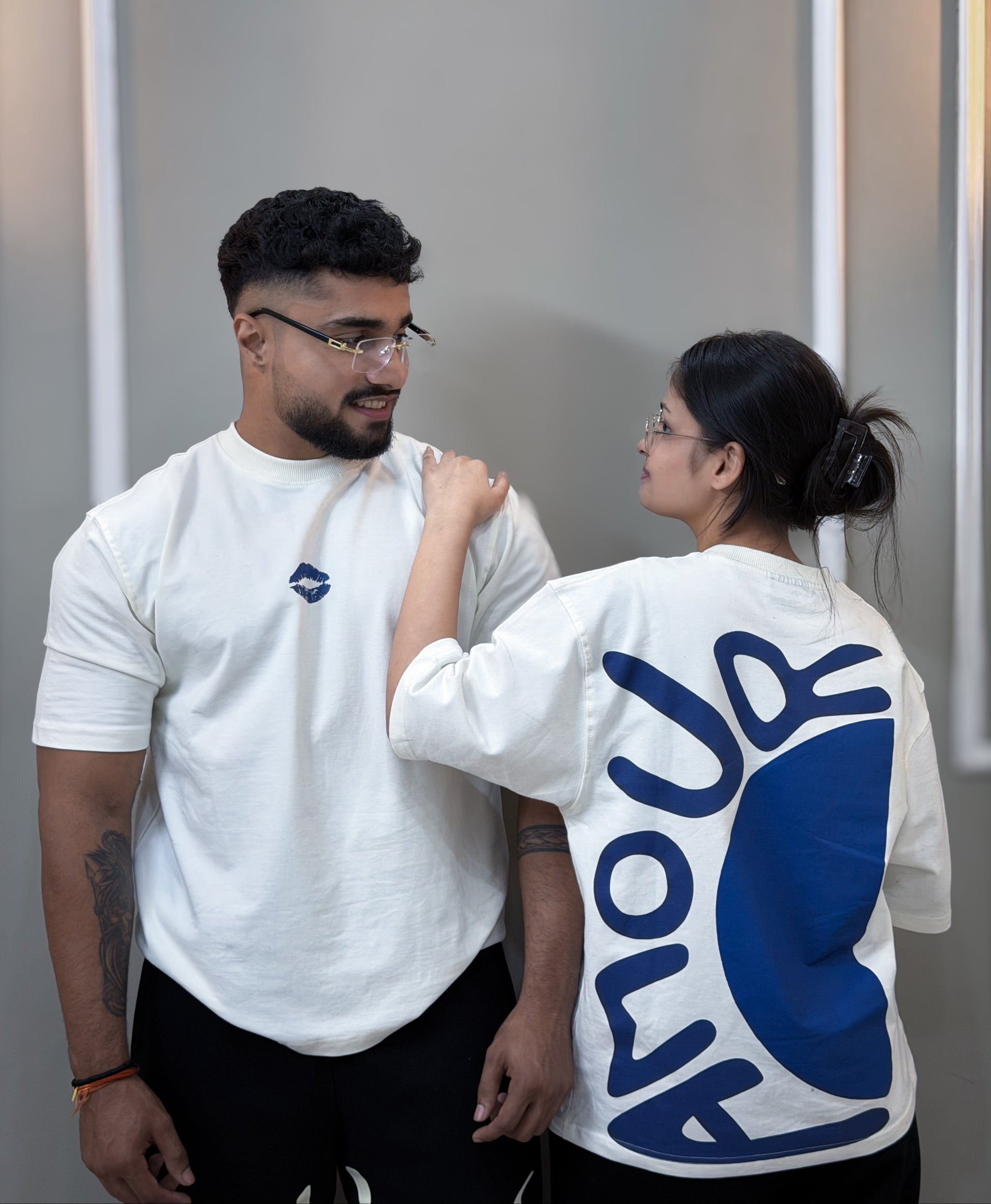 Two people wearing white t-shirts with a blue amour logo, one facing the camera and the other with their back to the camera.