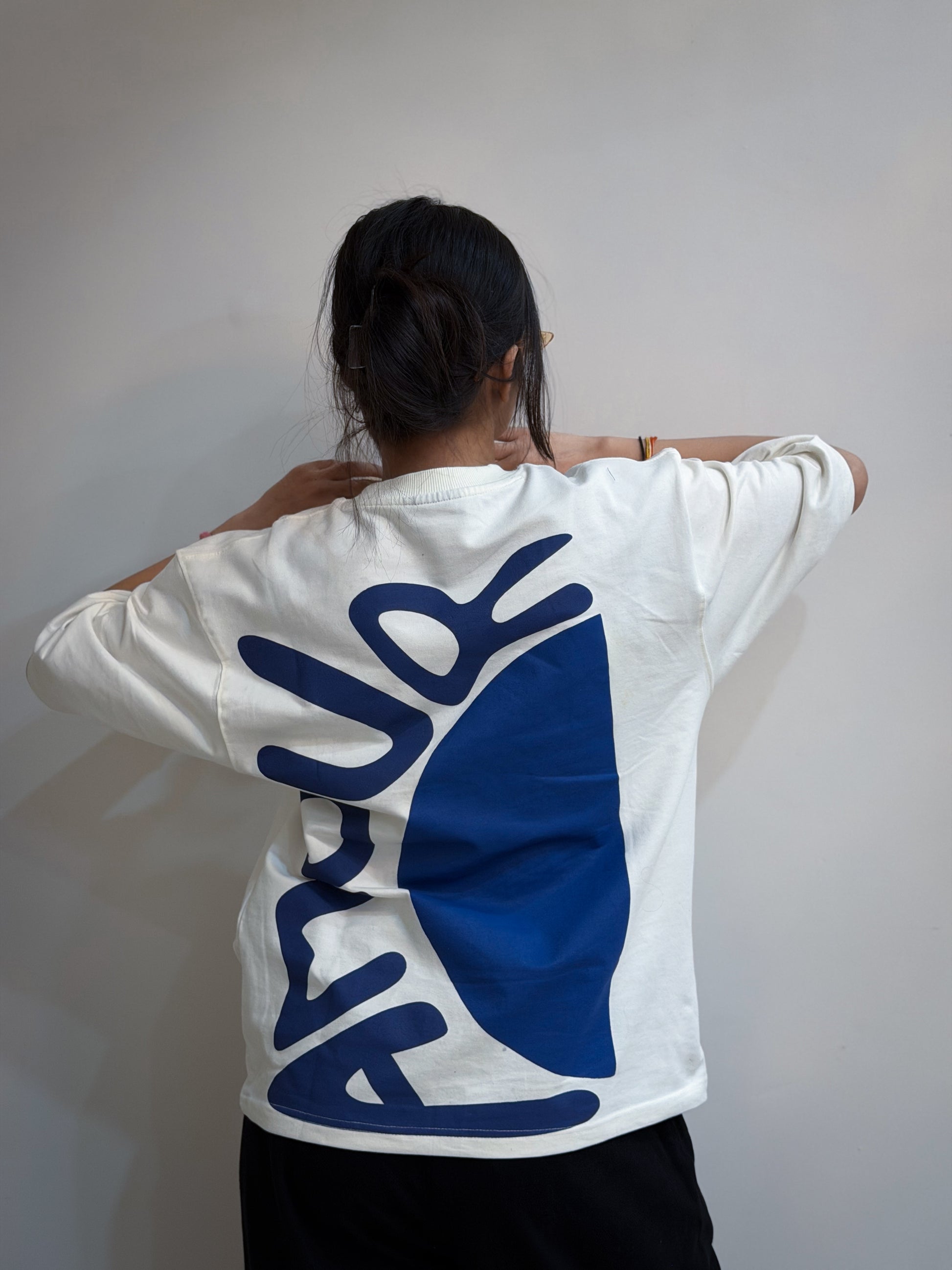 Person wearing a white sweatshirt with blue logo on the back against a plain background