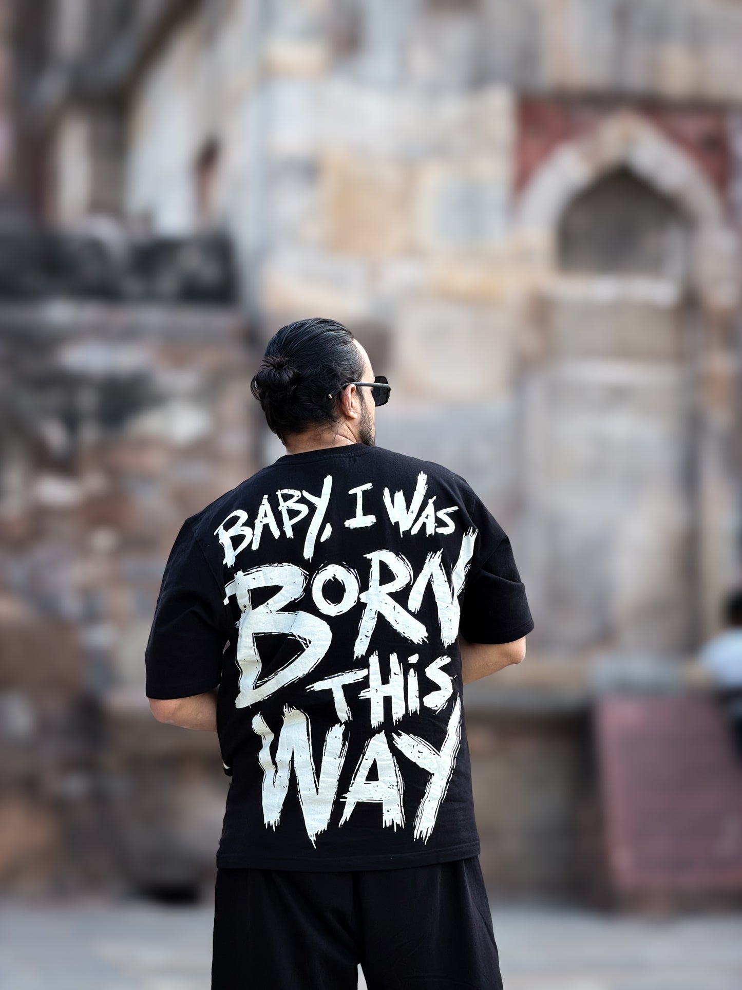 Person wearing a black t-shirt with white text "baby i was born this way" in an outdoor setting