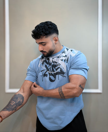 Man wearing a light blue t-shirt with a graphic design, standing against a neutral background.