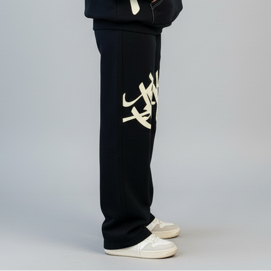 Black pants with a white logo worn by a person on a gray background